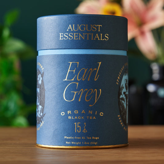 August Essentials Earl Grey organic black tea canister on a wooden surface with a blurred floral background
