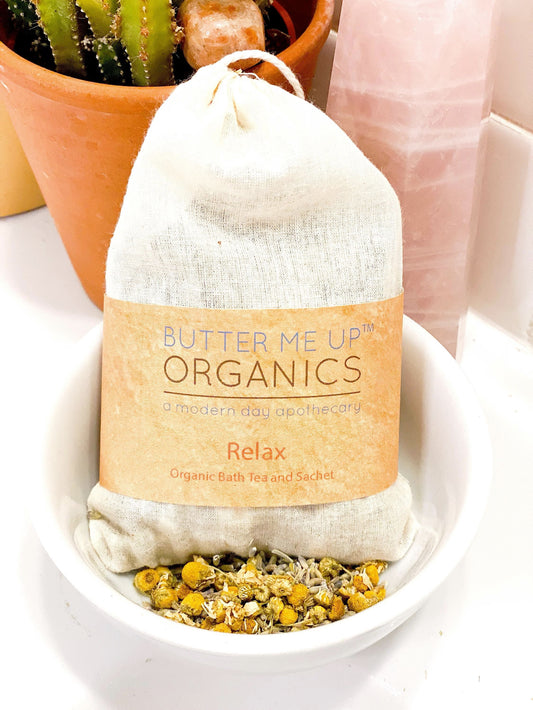 Butter Me Up Organics bath tea and sachet in a white bowl with a cactus plant in the background.