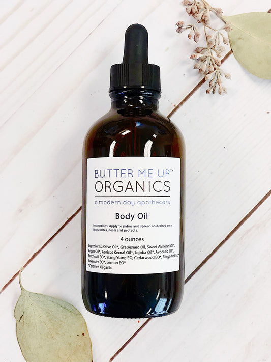 Butter Me Up Organics body oil bottle on a white background with leaves.