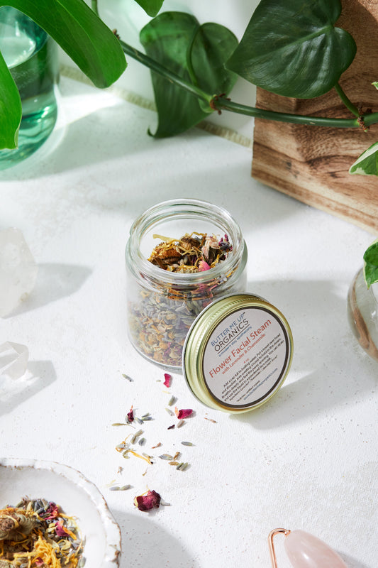 Jar of dried herbs with a label on a white surface with green leaves in the background