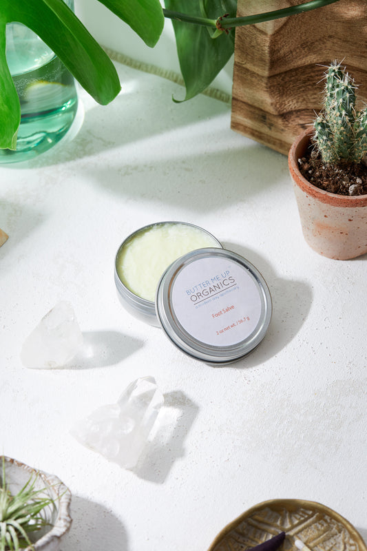 Cosmetic tin labeled 'Nature of Organics' on a white surface with plants in the background