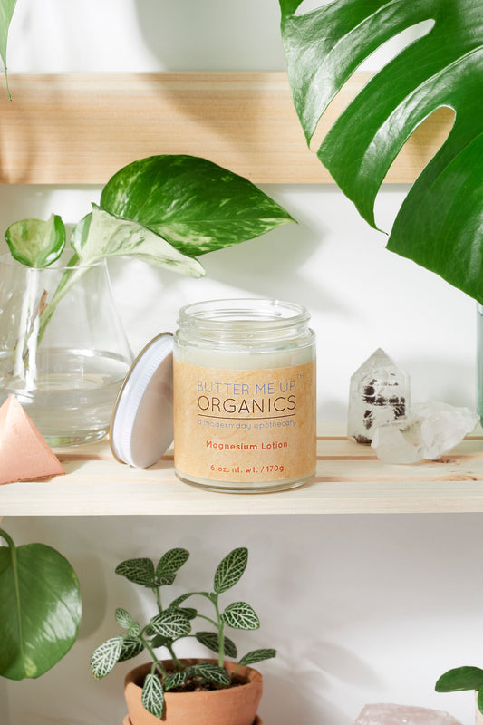 Candle labeled 'Better Me' Organics on a shelf with plants and crystals