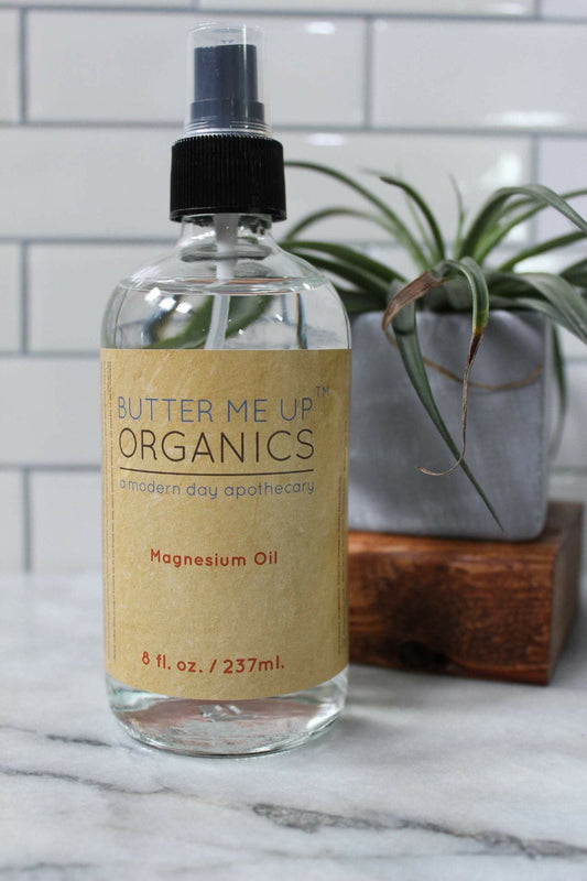 Bottle of Butter Me Up Organics magnesium oil on a marble surface with a plant in the background.