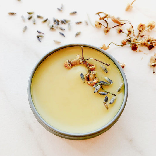 Candle in a gray container with dried flowers and herbs on a light background