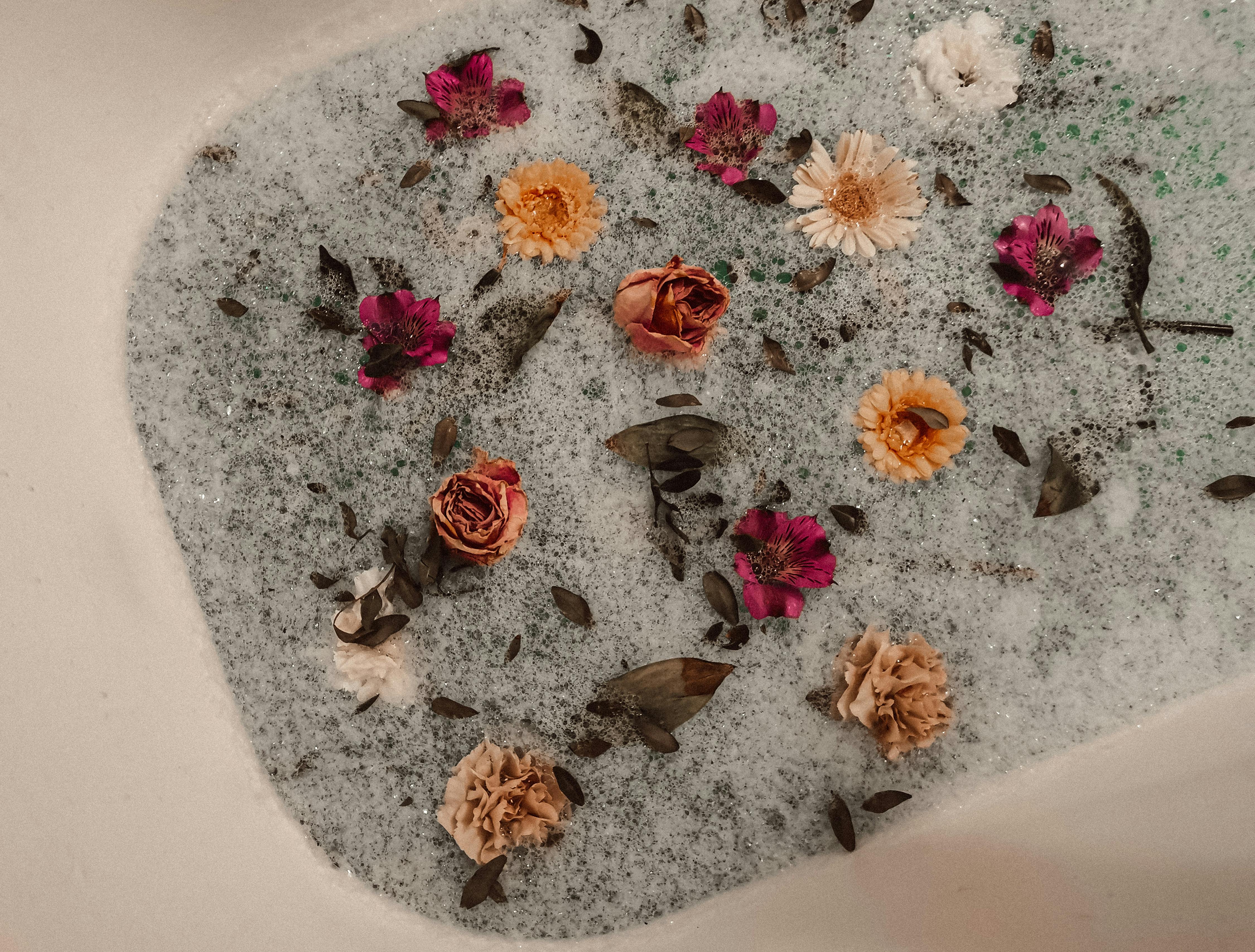 Relaxing floral bath with floating dried flowers, botanical petals, and foamy water in calming spa-inspired setting