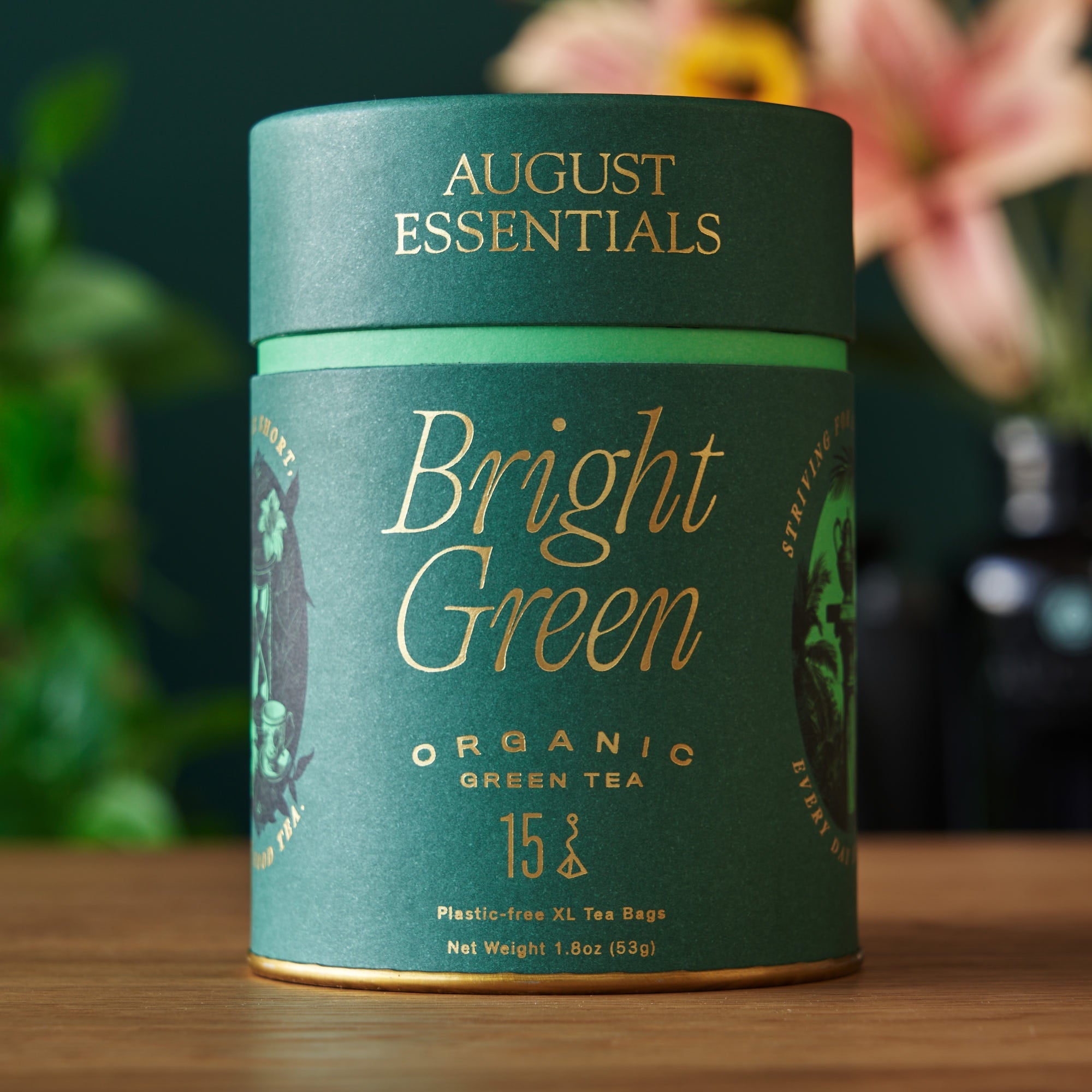 Green tea canister labeled 'Bright Green' by August Essentials on a wooden surface with blurred floral background