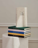 Stack of books titled 'The Five Minute Journal' on a pedestal against a neutral background