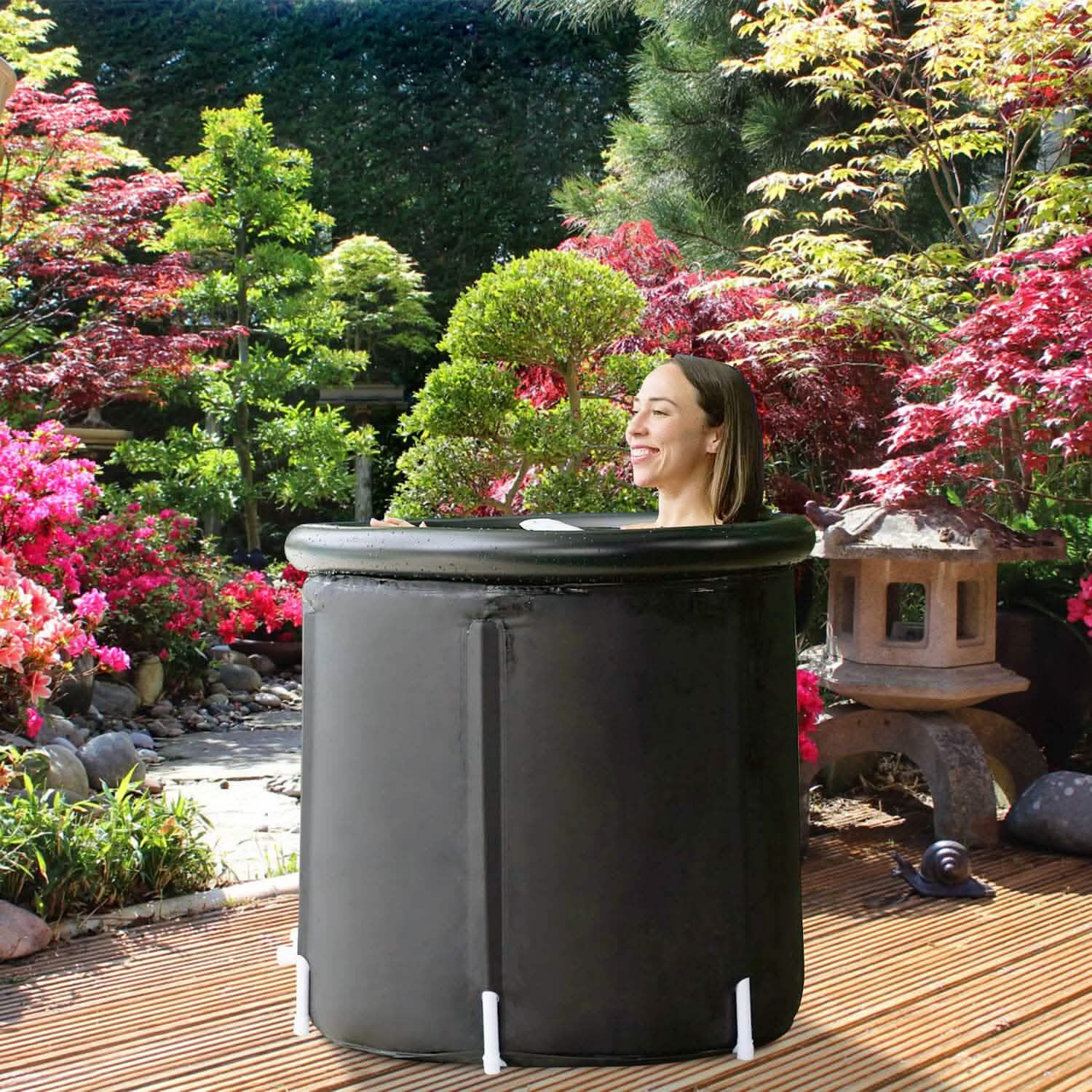 Person sitting in a portable hot tub surrounded by a garden with flowers and trees.
