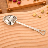 Metallic tea strainer on a wooden surface with dried flowers.