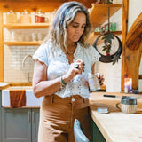Woman in a kitchen holding a container of cream or lotion.