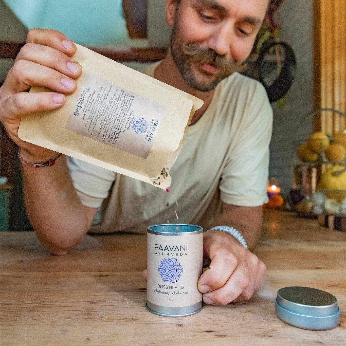 Man holding a Paavani Ayurveda tea package with a can of tea on a wooden table.