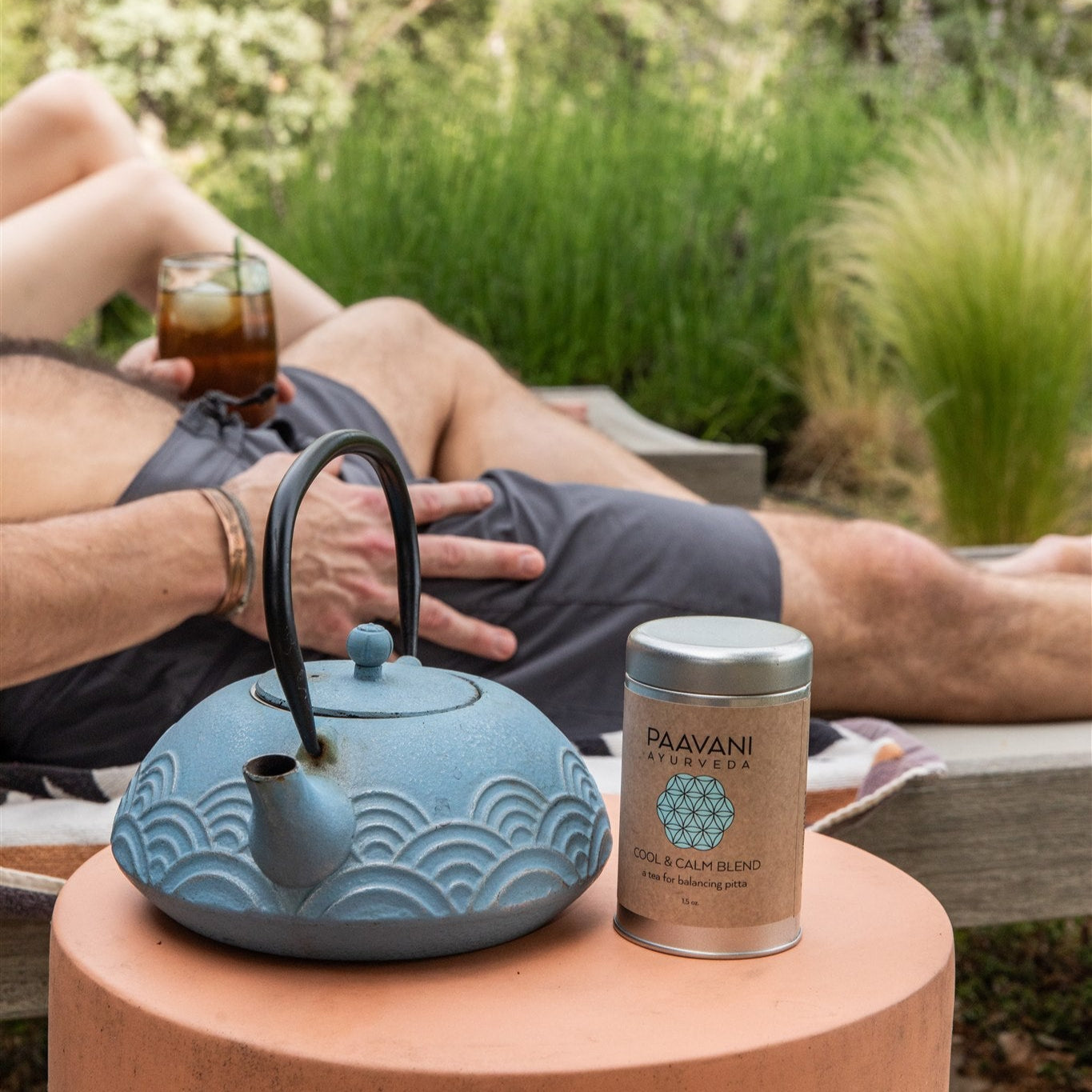 Person relaxing outdoors with a blue teapot and Paavani Ayurveda tea canister.