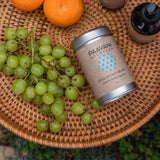 Paavani Ayurveda tea canister with grapes and oranges on a woven surface
