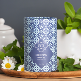 Blue patterned tea canister labeled 'Sleeping' on a wooden tray with greenery