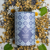 Tea canister labeled 'Sleeping Herbal Tea' surrounded by dried herbs and flowers.