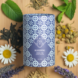 Blue tea canister labeled 'Sleeping Herbal Tea' surrounded by dried herbs and flowers on a wooden surface.