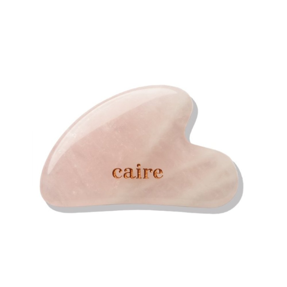 Pink gua sha tool with 'caire' branding on a white background