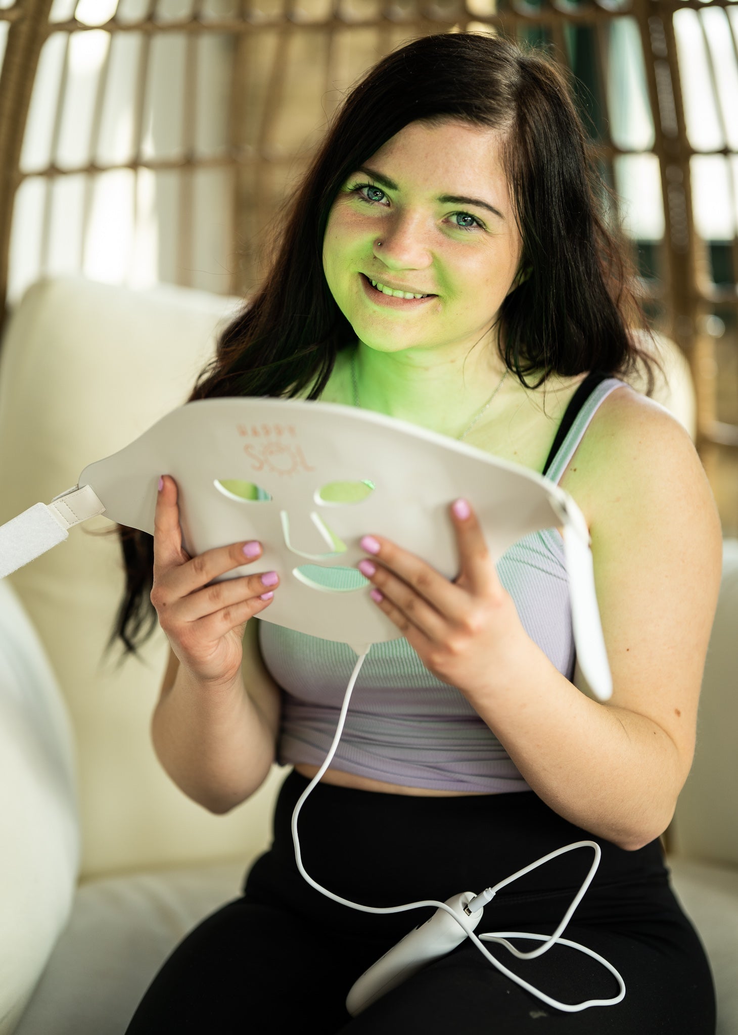 Woman holding a white electronic device with green light on a blurred indoor background
