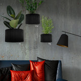Three black wall planters with plants against a gray concrete wall, with a sofa and pillows in the foreground.