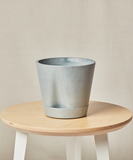 Gray ceramic planter on a wooden stool against a beige background